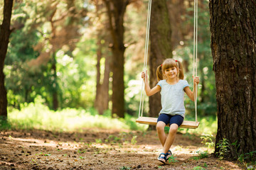 Happy Little girl on a swing in the summer park