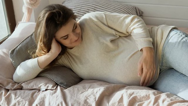 Happy pregnant lady lying on sofa hearing soft movement of her child in belly