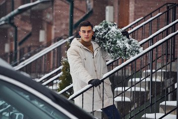 Man with christmas tree standing on the ladder of building