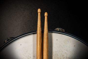 Close-up of two wooden drumsticks on an old metallic snare drum with dark background. Percussion...