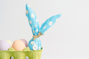 Easter background. Easter eggs painted with pastel colors on a light background next to an egg in a gift box resembling an Easter rabbit