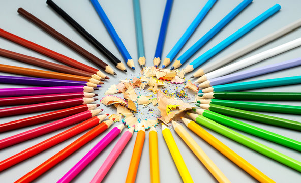 Multicolored pencils are arranged in a circle shape with wooden chips in the center