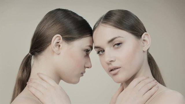 Faces of two twin girls in with nude makeup are looking at the camera. In the studio on a beige background. Natural beauty. Sisters. Skin care cosmetics.