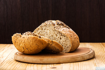 Loaf of wheat bread sprinkled with various seeds, with a cut slices of bread on a wooden table
