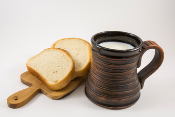 Fresh milk in a clay mug and pieces of bread on a wooden cutting board