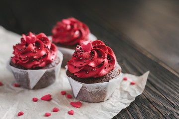 Valentine cupcakes in red color, decorated with sweet hearts on dark wooden table.