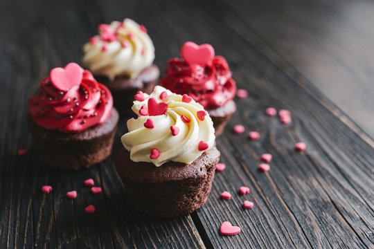 Valentine cupcakes in white and red colors, decorated with sweet hearts on a dark wooden table.