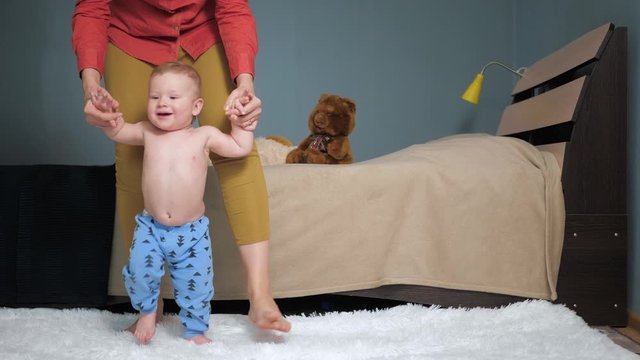 Mom leads baby holding his hands forward to camera. First baby steps concept. Slow motion