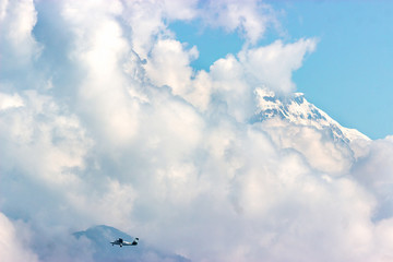 a small plane flies against the background of huge snow-capped mountain peaks. Lots of clouds and space for copyspace