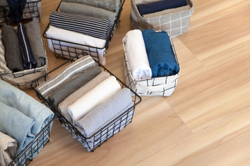 Obraz na płótnie Canvas Vertical tidying up storage. Neatly folded clothes neutral colors in the metal black baskets for wardrobe. Wooden background. Nordic style.