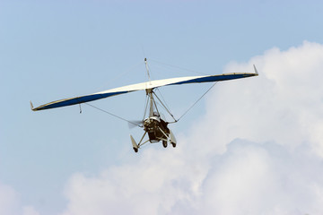 ultralight aircraft flies with people inside on a background of sky and clouds