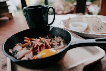 Traditional Asian fried egg pan, served on a wooden table with sliced ​​breads and coffee.