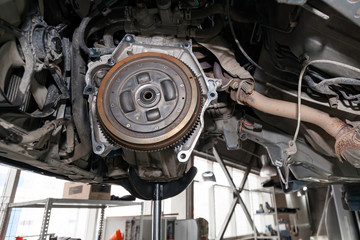 A car raised on a lift for repair and under it a detached Transmission gearbox suspended on a crane and a gear box on a lifting in a vehicle repair shop with view to the bottom in vehicle workshop.