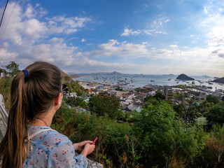 A girl in sunglasses standing on top of a hill in Labuan Bajo, Flores, Indonesia, and enjoying the view on the harbour. There are few islands in the back. The girl is daydreaming. Happiness and beauty