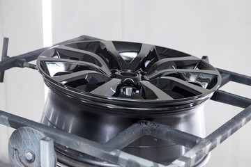A black painted aluminum alloy wheel is mounted on a special frame during drying in a chamber in a vehicle body repair workshop. Auto service industry.