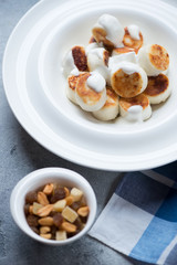 Close-up of fried vareniki or curd dumplings served with sour cream in a white plate, selective focus