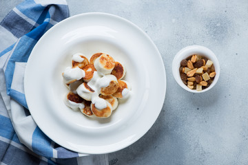 White plate with roasted curd dumplings or vareniki and sour cream, above view over light-blue stone background