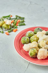 frozen brussels sprouts and broccoli cabbage green beans asparagus and carrots on a red plate in the kitchen