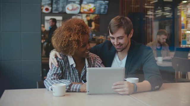 African young woman and caucasian man couple in cafe looking at a tablet screen