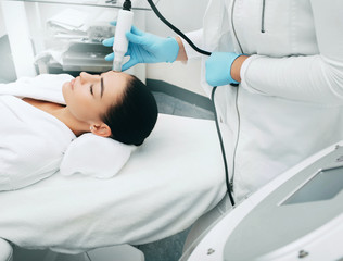 Beautician using machine no-needles mesotherapy smoothes wrinkles of the skin of the female forehead . Painless skin rejuvenation method