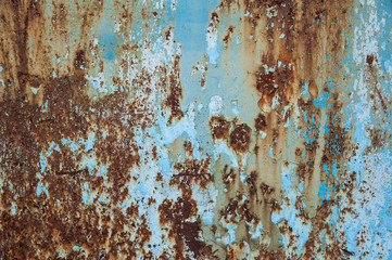 The remnants of light blue paint on a heavily corroded old metal surface. Abstract background, texture.
