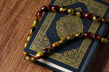 The Quran with rosary beads or &ldquo;tasbih&rdquo; and compass on wooden surface. Arabic characters means : Holy Quran, the Holy book of Islam. Islamic concept.