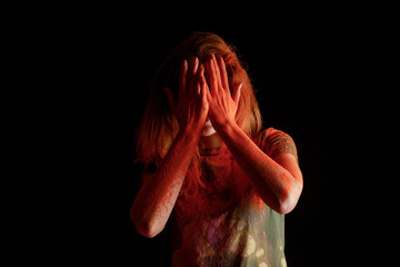 woman covering face with orange colorful holi paint on hands on black background
