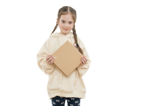 Cheerful little girl with pigtails dressed in hoodie holds cardboard box in hands and looking at the camera, isolated over white background, copyspace