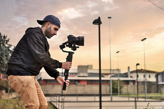 Caucasian videographer filming with cinema gimbal video dslr at sunset , professional video, videographer in event. Cinema lens on gimbal. Medium shot from right side