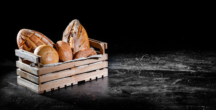 Fresh baked bread in wooden box on dark background