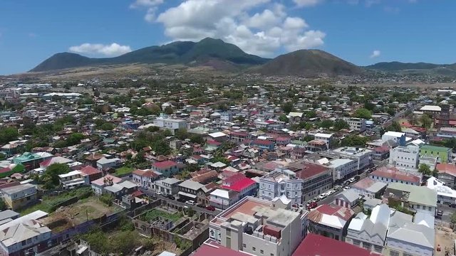 The Beautiful and Peaceful City Of Saint Kitts and Nevis Composed Of Unique Buildings and Trees With Green Rocky Mountains In The Background - Aerial Shot