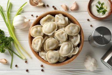 Bowl with tasty dumplings and spices on wooden background, top view