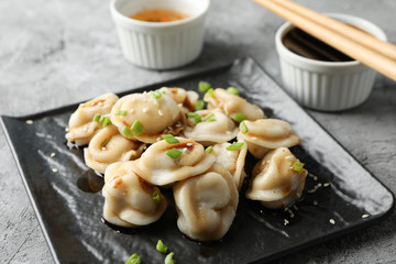 Square plate with dumplings, sauces and chopsticks on grey background, close up
