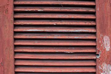 Close up of a dirty old red wooden window shutter with weathered and cracked paint
