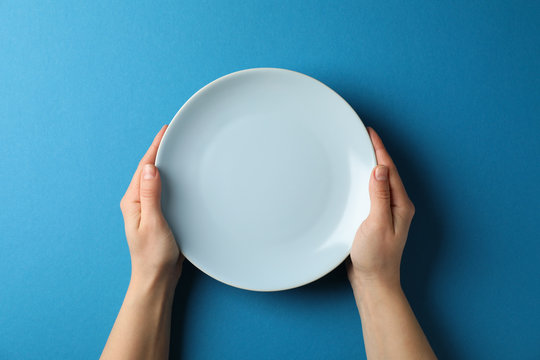 Female hands hold plate on blue background, top view