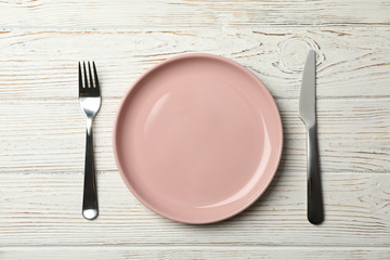 Plate, fork and knife on wooden background, top view