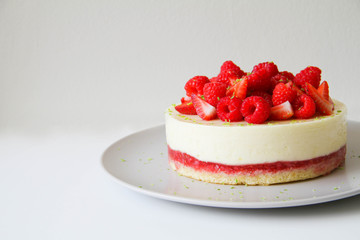 French dessert. Lime mousse cake with lime biscuit and red berries filling. Cake decorated with fresh berries and a lime zest. Cake is on a light grey plate, on a light background. 