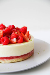 French dessert. Lime mousse cake with lime biscuit and red berries filling. Cake decorated with fresh berries and a lime zest. Cake is on a light grey plate, on a light background. 
