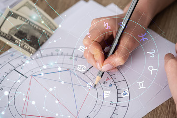 Cropped view of astrologer drawing natal chart beside dollar banknotes and constellations