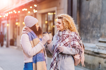 Outdoors fashion portrait of company cheerful pretty girls friends drinking coffee. Walking in the city. Talking and going shopping. Wearing stylish outerwear