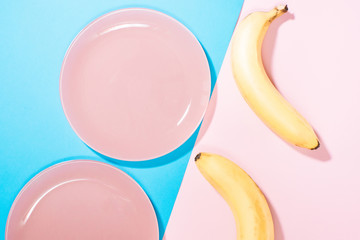 two pink plates and two bananas on a pink blue background. the view from the top Lay Flat. the concept of Breakfast, healthy food. keto diets. free space for text, copy space, minimalism