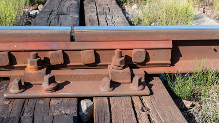 Closeup of a rusty railway track joint on wooden ties fastened with chair screws. Transport infrastructure. Railroad thermal expansion gap. - obrazy, fototapety, plakaty