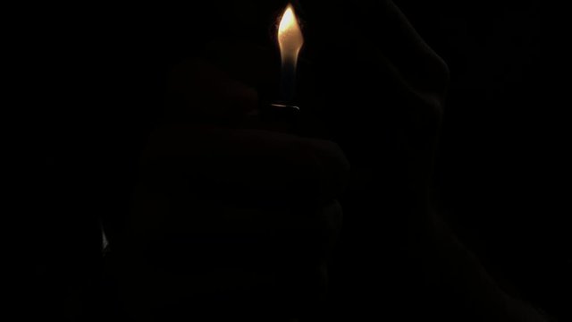 Man lighting up the cigar in total darkness with a lighter and smoking it. Man smoking a cigar at night. 