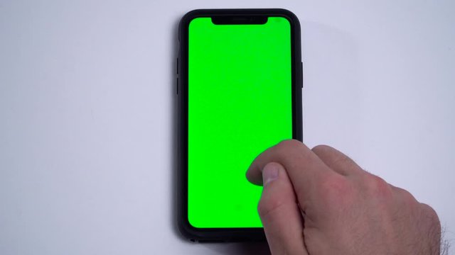 A man's hand using a smartphone with blank green screen zooming in and scrolling down. Vertical position isolated on a white background. 