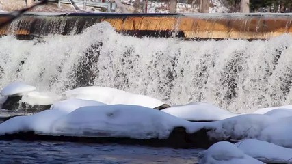 cold rushing water falls over frozen dam. Stationary medium shot - Powered by Adobe