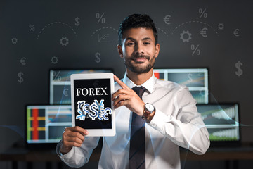 happy bi-racial trader holding digital tablet with forex letters