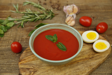 gazpacho spanish tomato soup topped with basil and tomatoes and garlic and egg on wooden rustic background. Cold soup. The concept of national cuisine.