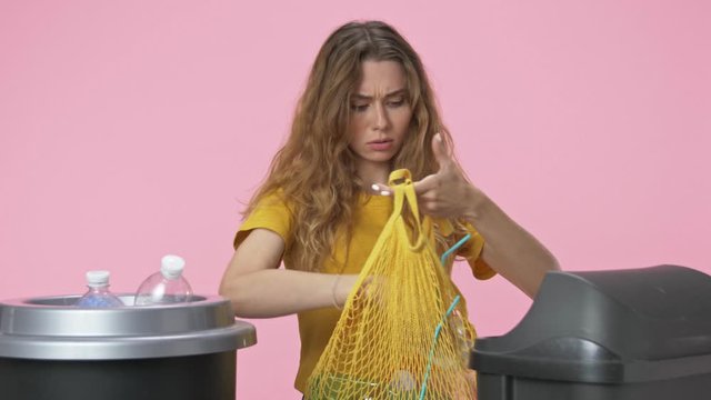 A pretty young woman is sorting garbage isolated over pink background