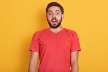 Obraz premium Close up portrait of astonished bearde male, posing isolated over yellow background, handsome man standing with widely opened mouth, young guy wearing red casual t shirt. People emotions concept.