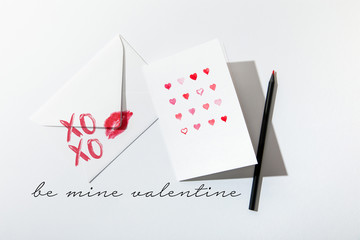 Fototapeta na wymiar top view of greeting card with hearts near envelope with lip print near be mine valentine lettering on white background